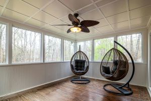 Sunroom featuring hanging egg chairs, wooden floor, and ceiling fan overlooking forest.