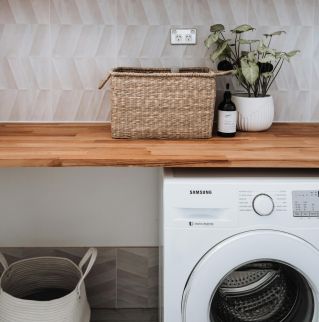 Bright and tidy laundry room featuring a washing machine, wicker basket, and potted plant on a wooden counter.